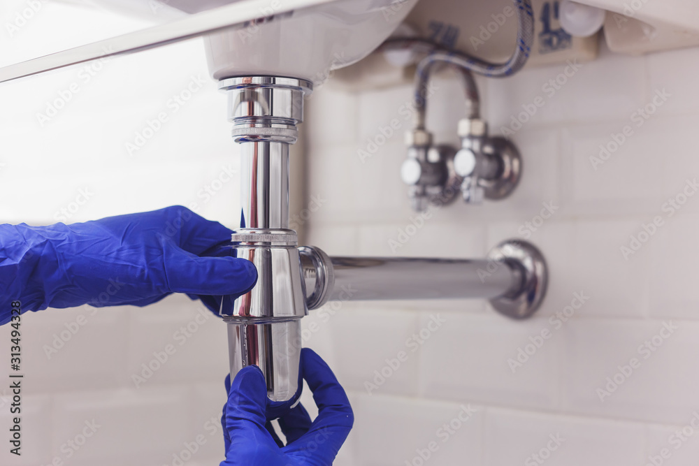Plumber repairs and maintains chrome siphon under the washbasin. Plumber at work in bathroom, plumbing assemble and install concept Plumber repairs and maintains chrome siphon under the washbasin. Plumber at work in bathroom, plumbing assemble and install concept