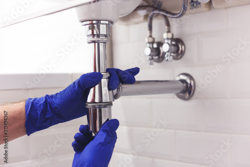 Obraz na płótnie Plumber repairs and maintains chrome siphon under the washbasin. Plumber at work in bathroom, plumbing assemble and install concept w salonie
