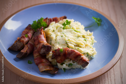 Beef liver wrapped in bacon with mash potato on blue table. horizontal image