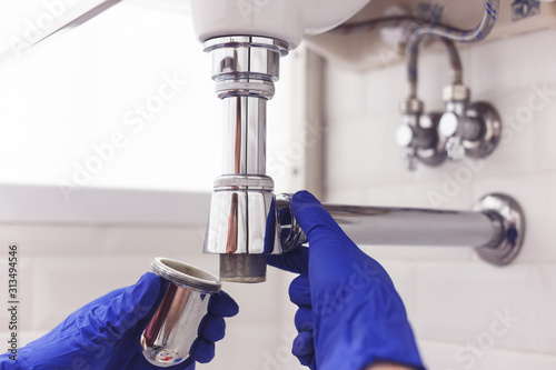 Obraz na płótnie Plumber repairs and maintains chrome siphon under the washbasin. Plumber at work in bathroom, plumbing assemble and install concept w salonie