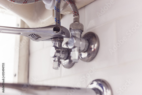 Plumber turns nut on angle valve under wash basin using spreading wrench. photo