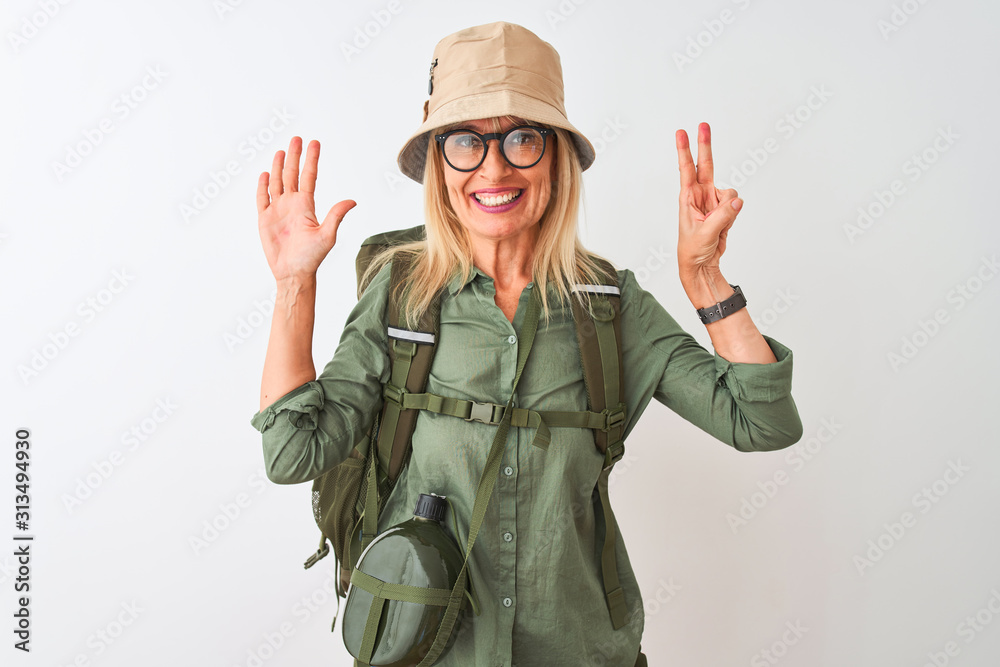 Middle age hiker woman wearing backpack hat canteen glasses over isolated white background showing and pointing up with fingers number seven while smiling confident and happy. Middle age hiker woman wearing backpack hat canteen glasses over isolated white background showing and pointing up with fingers number seven while smiling confident and happy.