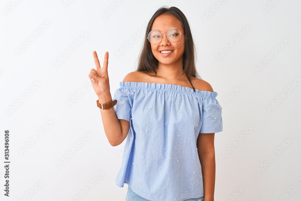Young chinese woman wearing blue t-shirt and glasses over isolated white background showing and pointing up with fingers number two while smiling confident and happy. Young chinese woman wearing blue t-shirt and glasses over isolated white background showing and pointing up with fingers number two while smiling confident and happy.