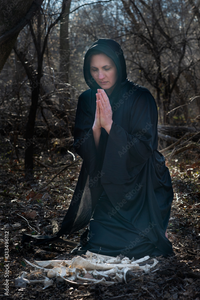 Woman in black robes with pile of large wild animal bones in the middle of the forest. Magic and Witchcraft concept. Woman in black robes with pile of large wild animal bones in the middle of the forest. Magic and Witchcraft concept.