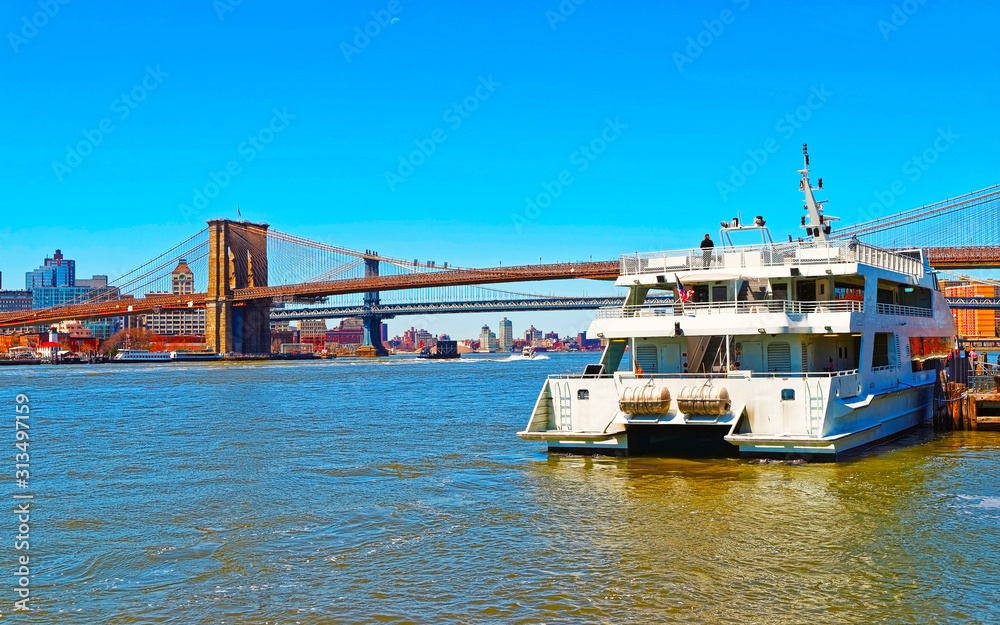 Ferry boat with Tourists and Brooklyn bridge across East River, New York, USA. It is among the oldest in the United States of America. NYC, US. Skyline and cityscape. American construction