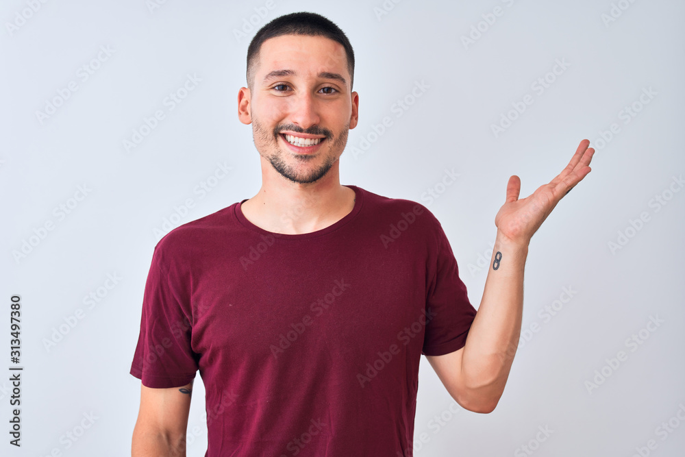 Young handsome man standing over isolated background smiling cheerful presenting and pointing with palm of hand looking at the camera.