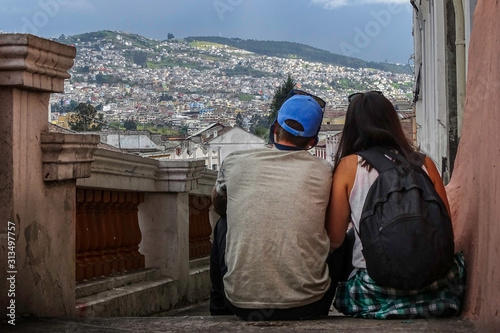A traveler couple sitting on old stairs of Quito old town, Ecuador. they are with their back turned and a beautiful mount landscape of the village can be seen behind.