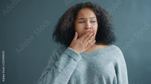 Portrait of tired and sleepy Afro-American lady yawning looking at camera indoors on dark gray background. Modern people and human gestures concept.