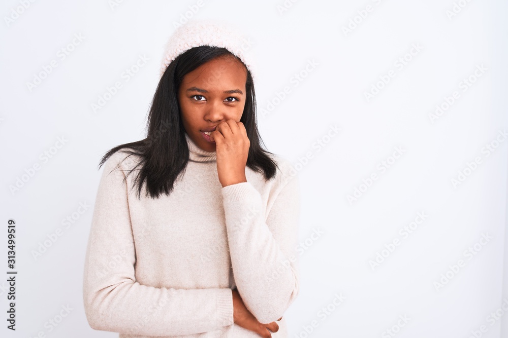 Beautiful young african american woman wearing turtleneck sweater and winter hat looking stressed and nervous with hands on mouth biting nails. Anxiety problem.