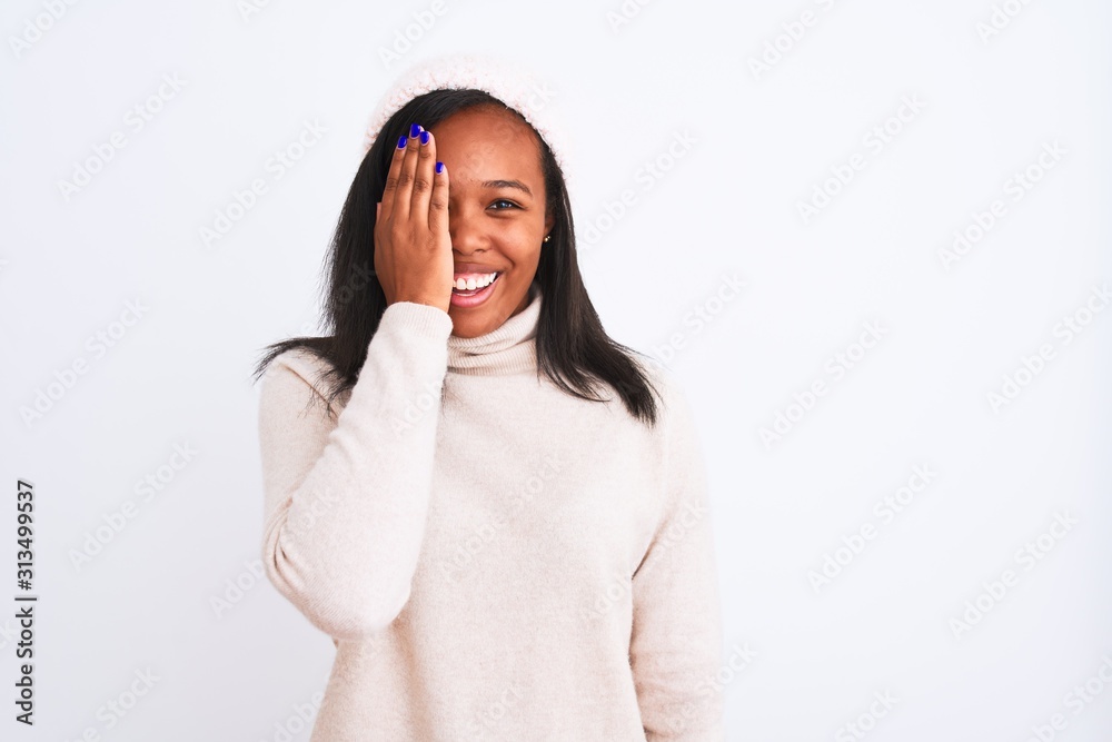Beautiful young african american woman wearing turtleneck sweater and winter hat covering one eye with hand, confident smile on face and surprise emotion. Beautiful young african american woman wearing turtleneck sweater and winter hat covering one eye with hand, confident smile on face and surprise emotion.