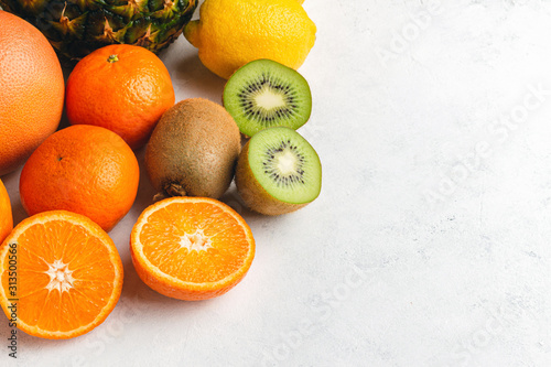 Assortment of tropical fruits, sliced and whole kiwi, orange, banana, tangerine, lemon, pineapple, grapefruit on textured white background © O.Farion
