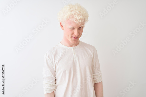 Young albino blond man wearing casual t-shirt standing over isolated white background winking looking at the camera with sexy expression, cheerful and happy face.