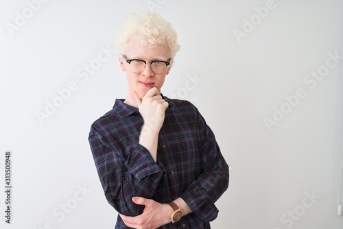 Young albino blond man wearing casual shirt and glasses over isolated white background looking confident at the camera smiling with crossed arms and hand raised on chin. Thinking positive.