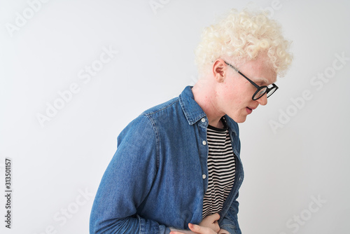 Young albino blond man wearing denim shirt and glasses over isolated white background with hand on stomach because indigestion, painful illness feeling unwell. Ache concept.