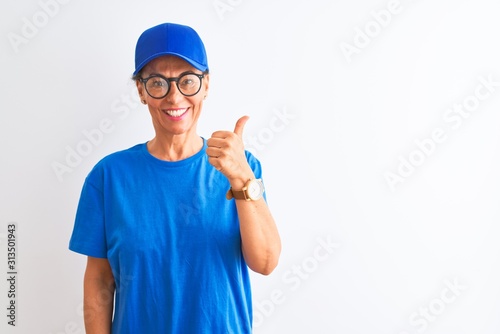 Senior deliverywoman wearing cap and glasses standing over isolated white background doing happy thumbs up gesture with hand. Approving expression looking at the camera with showing success.