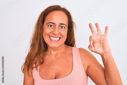Middle age mature woman standing over white isolated background doing ok sign with fingers, excellent symbol