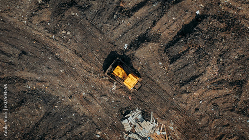 Aerial top view of a construction site or country dump with yellow excavator or bulldozer, heavy equipment, drone photo.