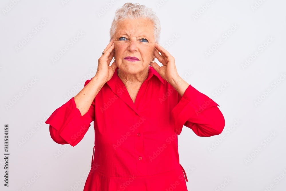 Senior grey-haired woman wearing red casual shirt standing over isolated white background covering ears with fingers with annoyed expression for the noise of loud music. Deaf concept. Senior grey-haired woman wearing red casual shirt standing over isolated white background covering ears with fingers with annoyed expression for the noise of loud music. Deaf concept.
