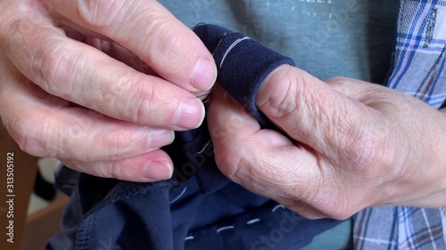 A senior elderly woman grandmother sewing fabric clothes with needle, hands close up