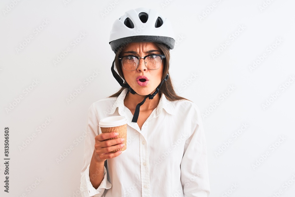 Beautiful businesswoman wearing bike helmet drinking coffee over isolated white background scared in shock with a surprise face, afraid and excited with fear expression Beautiful businesswoman wearing bike helmet drinking coffee over isolated white background scared in shock with a surprise face, afraid and excited with fear expression