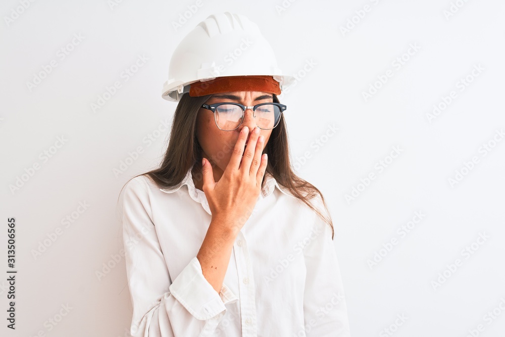 Young beautiful architect woman wearing helmet and glasses over isolated white background bored yawning tired covering mouth with hand. Restless and sleepiness.