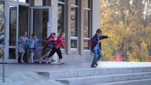 Happy primary school students opening school doors and running away from school building after lessons. Crowd of joyful preadolescent schoolkids leaving school at the end of studies and rushing home
