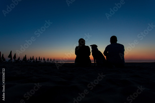 Family portrait silhouette with dog on a desert beach with closed umbrellas