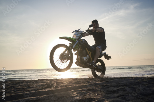 Man on the motorbike mke jump on the black sand beach against sun