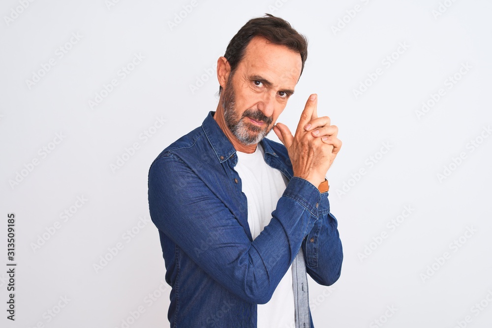 Middle age handsome man wearing blue denim shirt standing over isolated white background Holding symbolic gun with hand gesture, playing killing shooting weapons, angry face Middle age handsome man wearing blue denim shirt standing over isolated white background Holding symbolic gun with hand gesture, playing killing shooting weapons, angry face