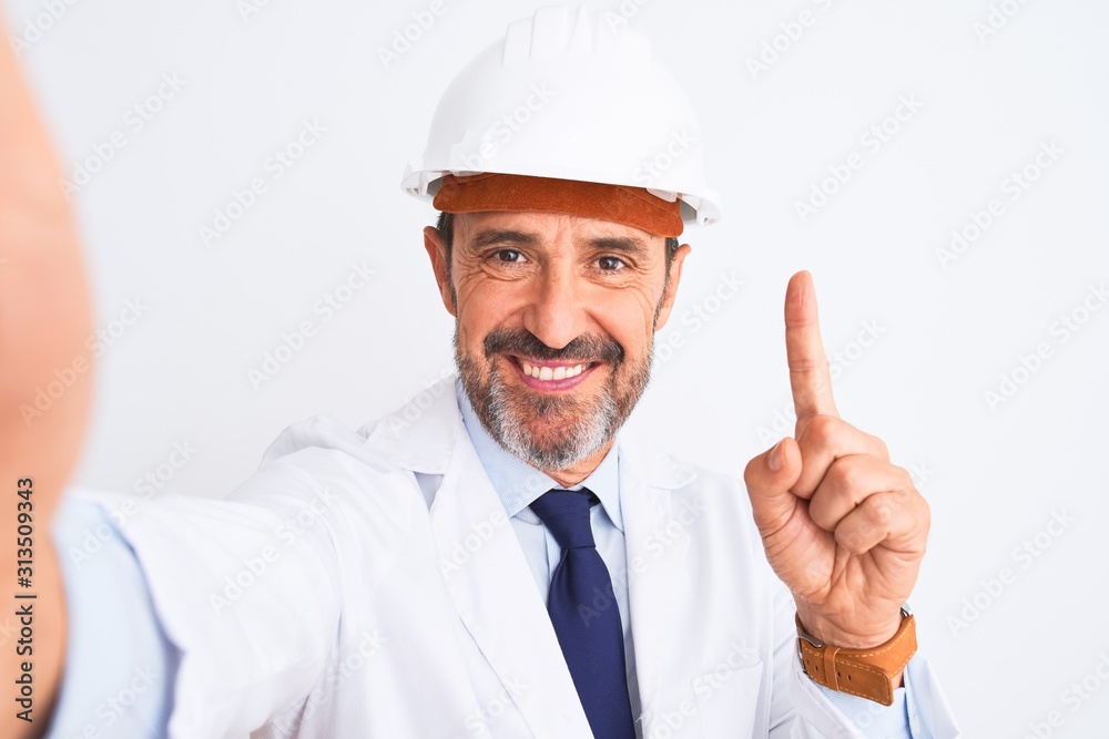 Middle age engineer man wearing helmet make selfie over isolated white background surprised with an idea or question pointing finger with happy face, number one Middle age engineer man wearing helmet make selfie over isolated white background surprised with an idea or question pointing finger with happy face, number one