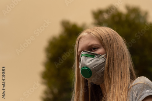 Australian bushfire: blond girl wearing P2 N95 protection respiratory mask to reduce amount of breathing PM2.5 particles from bushfire smoke.