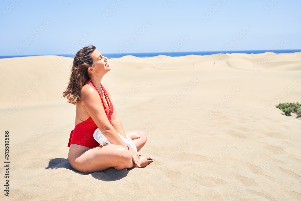 Young beautiful woman sunbathing and relaxing sitting on the sand doing yoga poses at maspalomas dunes bech