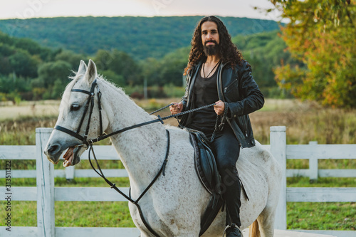 Handsome rider man on horse. Equestrian rides his white well looking horse. Handsome man riding horse at farm. Attractive male sitting on white stallion on the ranch in autumn.