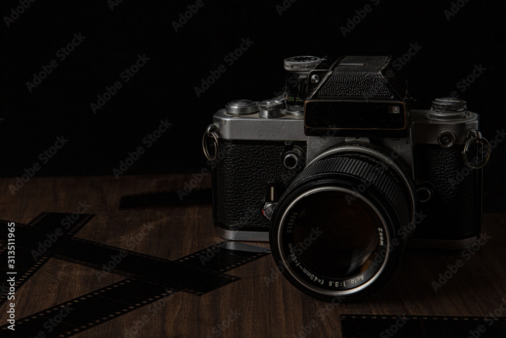 Vintage film camera on a wooden table and black background with film lens and camera shot in low key dark style