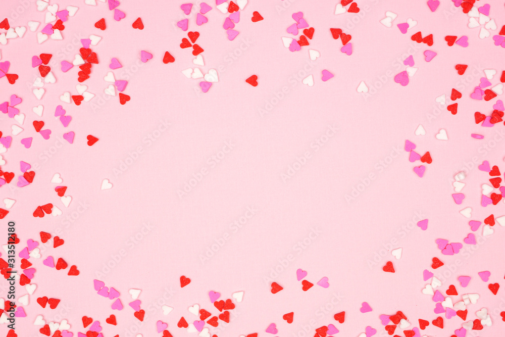 Valentines Day frame of candy heart sprinkles over a pink textured background. Copy space.