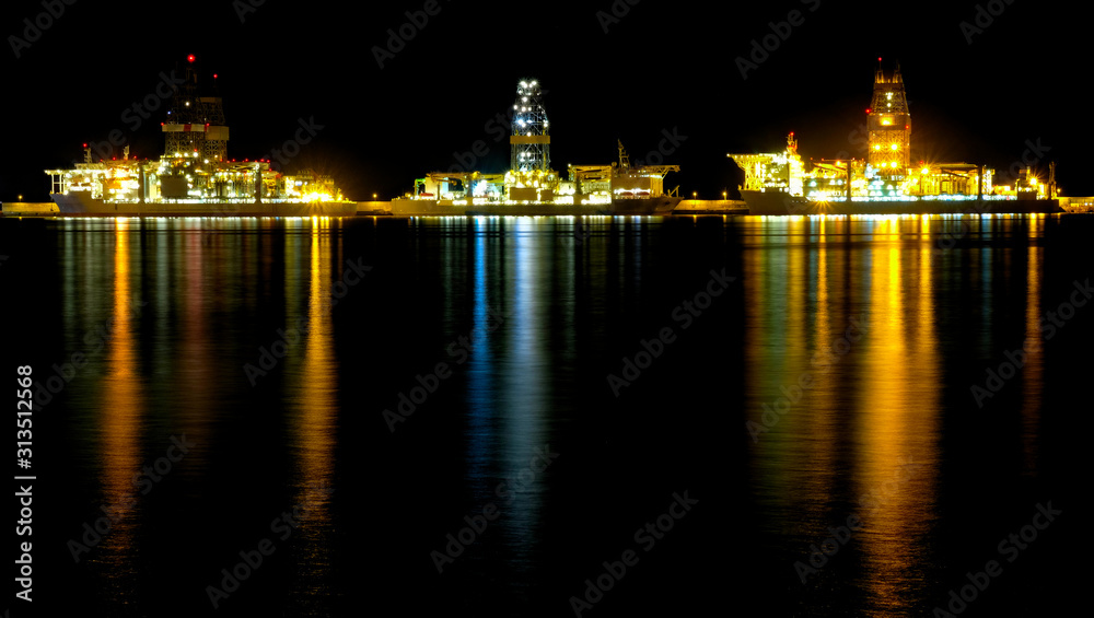 A big commercial harbor at night with oil rigs docked at a repair wharf.