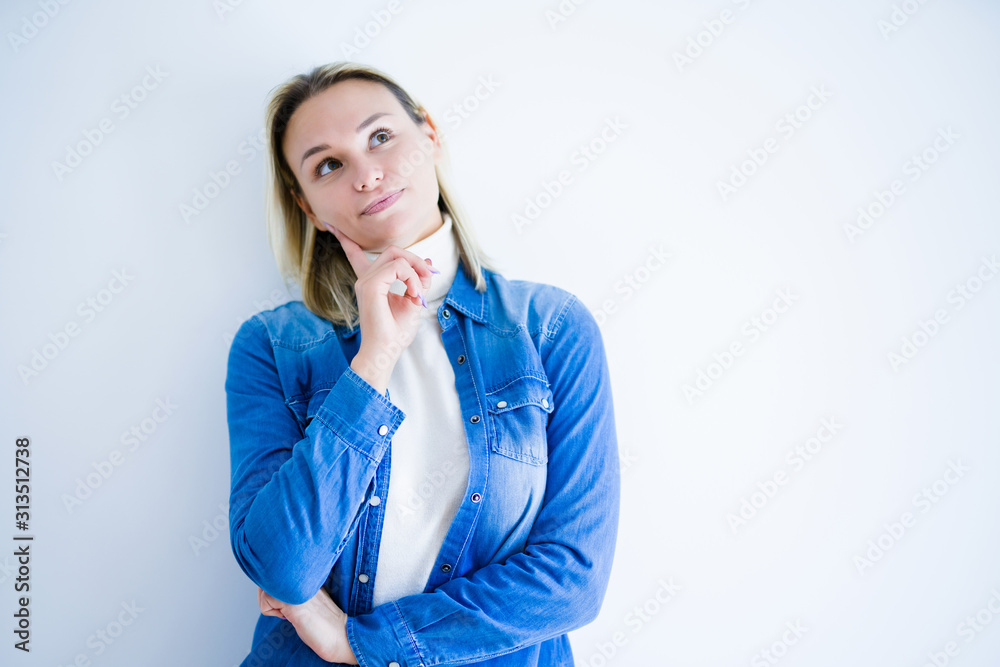 Young beautiful woman wearing denim shirt standing over isolated white background with hand on chin thinking about question, pensive expression. Smiling with thoughtful face. Doubt concept. Young beautiful woman wearing denim shirt standing over isolated white background with hand on chin thinking about question, pensive expression. Smiling with thoughtful face. Doubt concept.