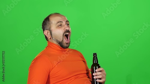 Caucasian man holds a bottle of beer in his hands and drinks with pleasure, green screen. Slow motion