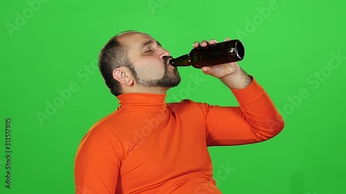 Caucasian man holds a bottle of beer in his hands and drinks with pleasure, green screen. Slow motion