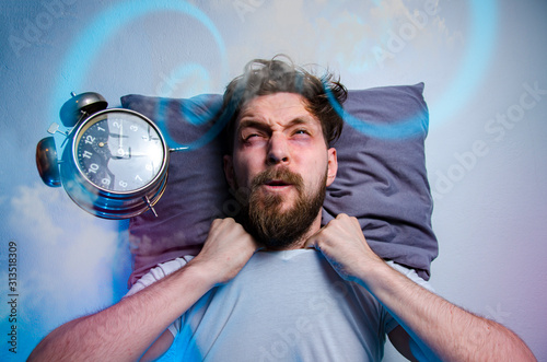 Mad man having trouble sleeping, insomnia concept, alarm clock flying in front of his head  photo