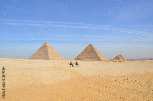 Tourists riding camel exploring the Giza Plateau with the Pyramids around.