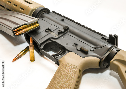 An multi colored AR 15 rifle with a rifle magazine loaded with 223 caliber bullets on it with two of the same bullets in front of it on a white background