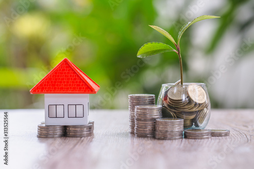 The orange roof houses put on piles of coins and coins in bottles with growing seedlings. Concepts of saving money, buying a house and mortgage, real estate and investing, buying a house For growth. photo