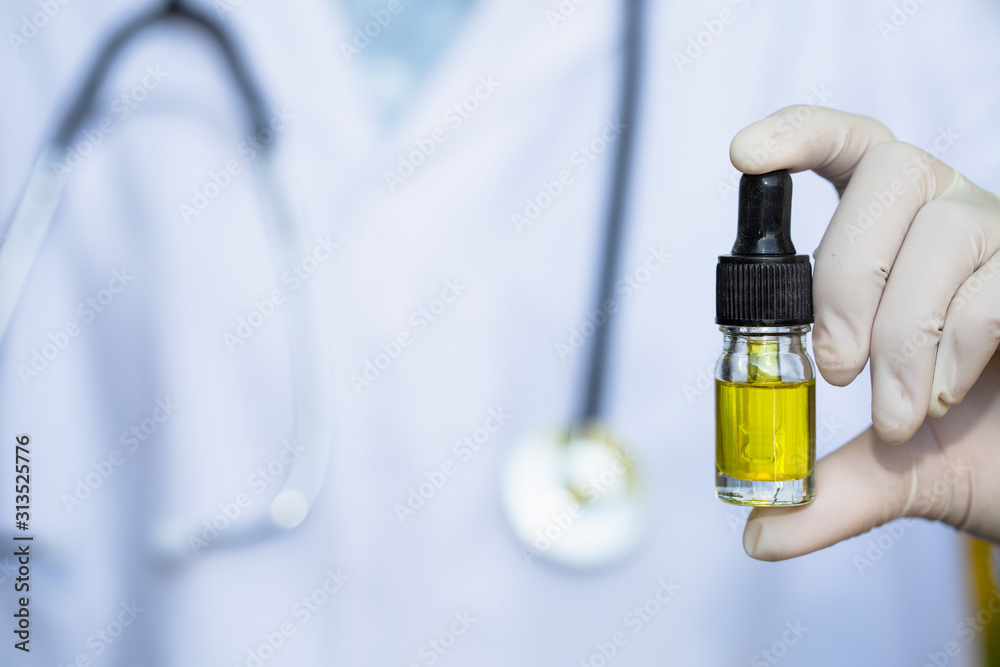 Glass bottle handle, CBD hemp oil. Doctors or researchers hold a bottle of hemp oil. Background with medical stethoscope.medical marijuana concept, CBD cannabis OIL. hemp product, close up Glass bottle handle, CBD hemp oil. Doctors or researchers hold a bottle of hemp oil. Background with medical stethoscope.medical marijuana concept, CBD cannabis OIL. hemp product, close up