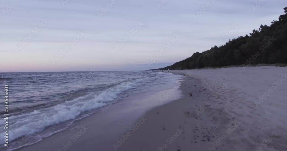A near-ground drone shot during a sunset on the beach.
You can see the waves on the beach and unrecognizable people taking a walk in the background. A near-ground drone shot during a sunset on the beach.
You can see the waves on the beach and unrecognizable people taking a walk in the background.