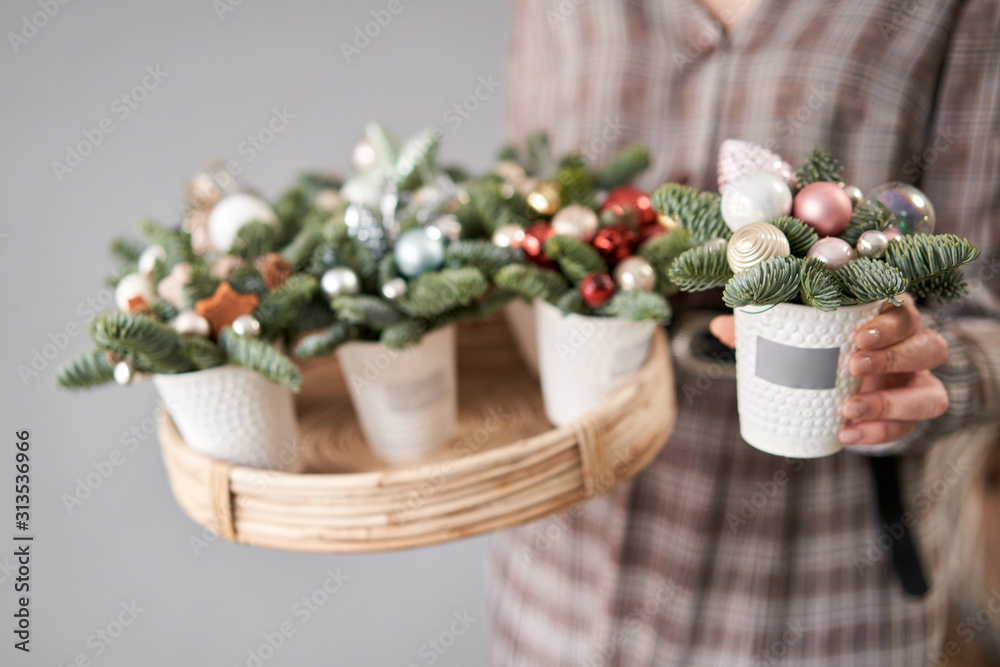 Florist holds a tray with christmas arrangements and one in his hand. Beautiful festive arrangement of fresh spruce in coffee Cup. Christmas mood.