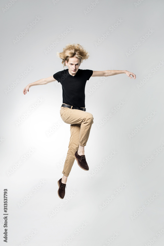 A frantic and expressive jump, hair scatter in different directions. Portrait of a jumping man on a light background.