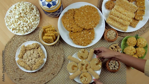 Top view shot of various Lohri items consumed during the winter season in India - Lohri festival. Indian woman hands placing a plate of til patti and gajak rolls on a wooden table surrounded by rew... photo