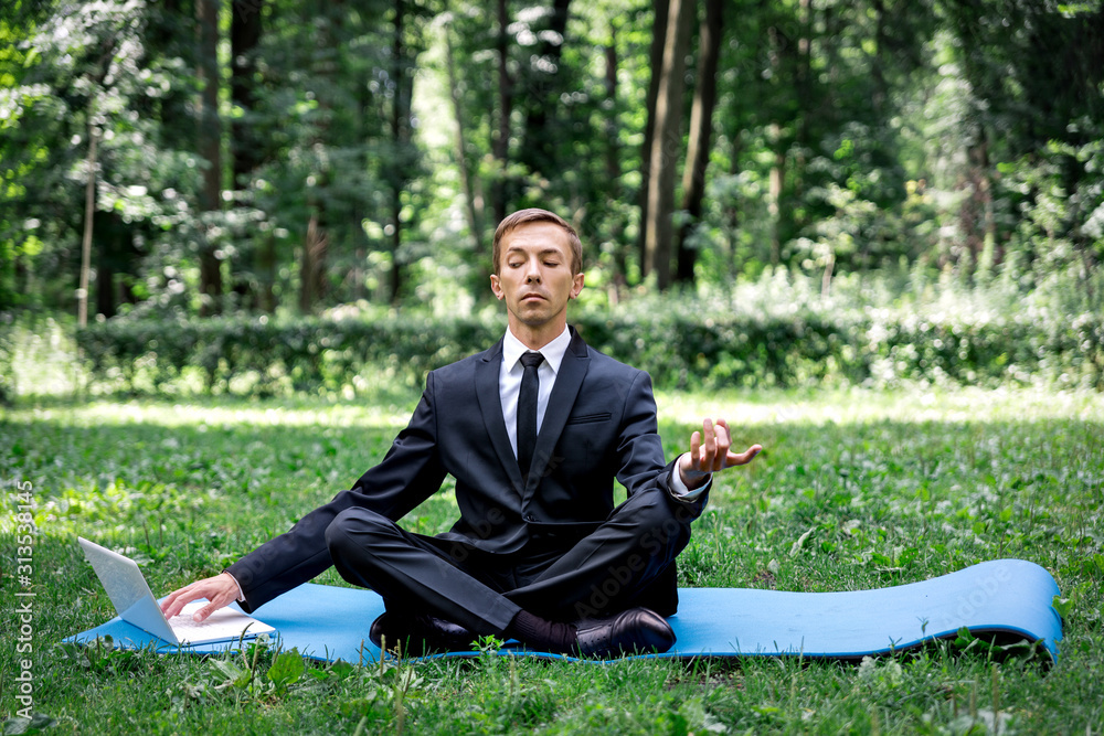 Man in a suit with tie. Business man relaxing in a park in the lotus position, he can't relax in any way, typing text on a computer with one hand. one eye mows into the monitor. Man in a suit with tie. Business man relaxing in a park in the lotus position, he can't relax in any way, typing text on a computer with one hand. one eye mows into the monitor.