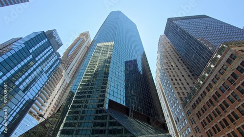 Manhattan cityscape, low angle panning view on New York City corporate skyscrapers with reflecting glass facades, clear blue sky sunny day